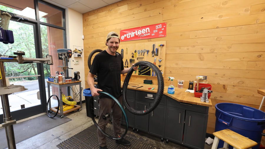 A mechanic in the e*thirteen workshop holding a Grappler Radial tire in one hand and a Flux rim in the other, ready to mount it.