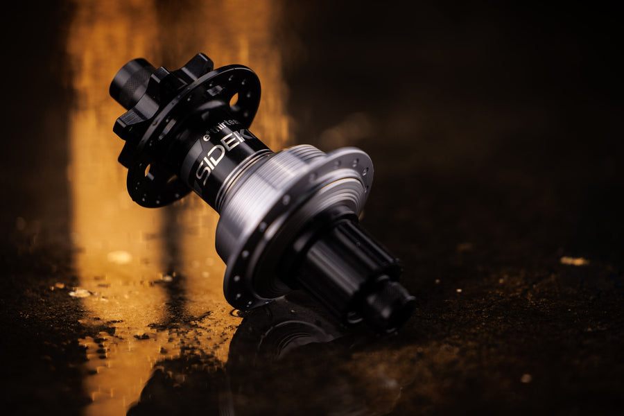 The first-generation Sidekick rear hub, black shell and silver freehub body, lying on wet ground in warm light.