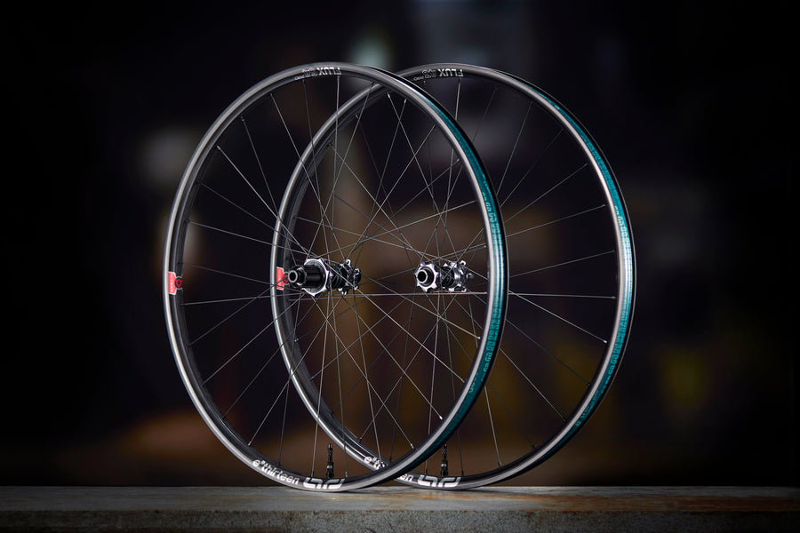 A Sidekick Flux front and rear wheel standing side by side on a dark floor, Flux rims with the teal rim-bed decal and Sidekick hubs.